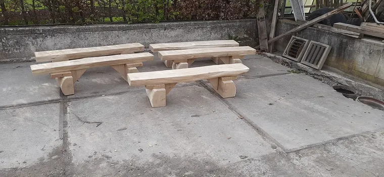 Drei massive Holzbänke ohne Lehne auf einem Betonhof.