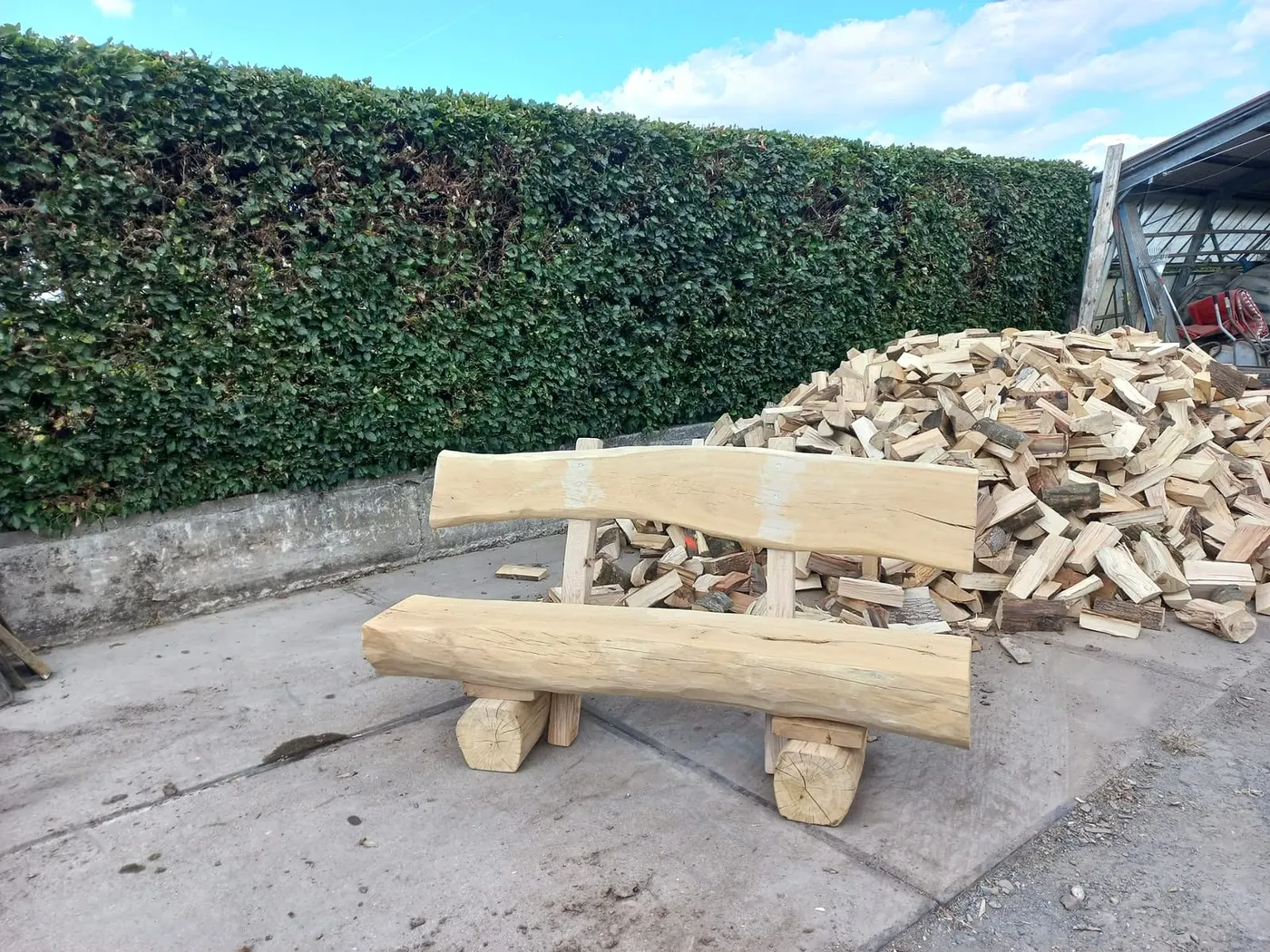 Massive Holzbank mit Lehne vor einem Haufen gespaltenem Kaminholz.