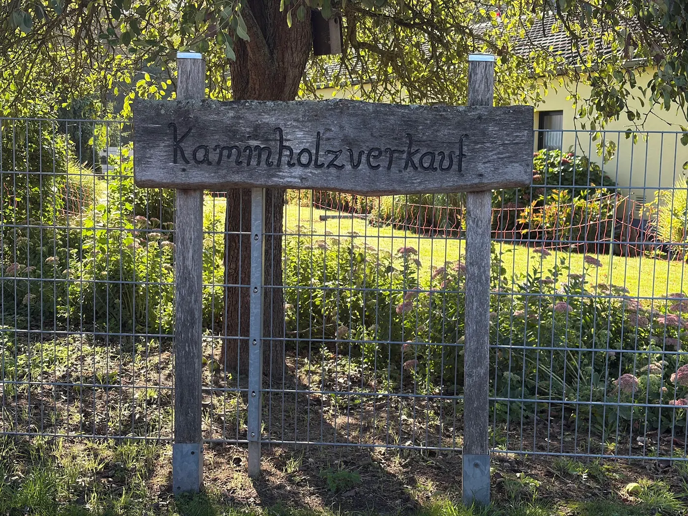 Geschnitztes Holzschild „Kaminholzverkauf“ am Zaun