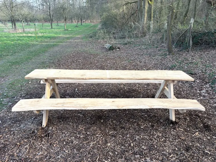 Lange Tisch-Bank-Garnitur aus Holz in Seitenansicht am Waldrand.